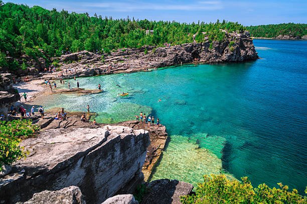 Scenic turquoise water of The Grotto with rocky cliffs and tourists at Bruce Peninsula National Park near Georgian Bay